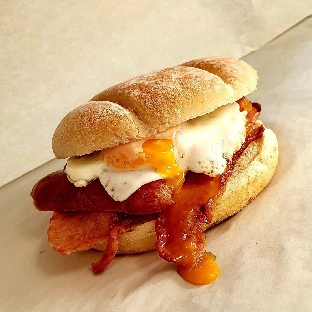A floury breakfast roll filled with bacon and a fried egg with a runny yolk